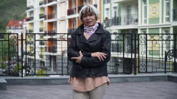 Visão frontal retrato confiante bela mulher magra sênior posando ao ar livre na rua da cidade. Média tiro charmoso aposentado caucasiano em óculos olhando para a câmera sorrindo. Estilo de vida e confiança. — Vídeo de Stock