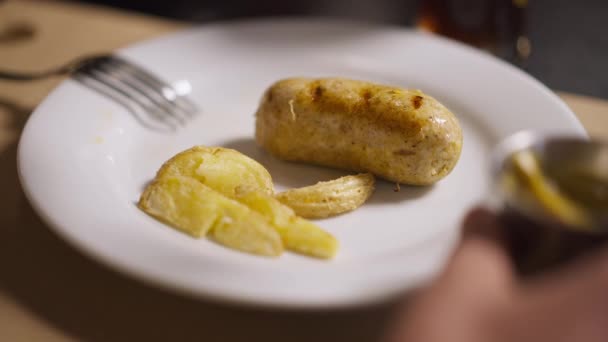 Placa de jantar close-up com mão masculina espalhando molho de mostarda em salsicha assada grelhada em câmera lenta. irreconhecível masculino caucasiano cliente jantar no almoço no restaurante dentro de casa. — Vídeo de Stock