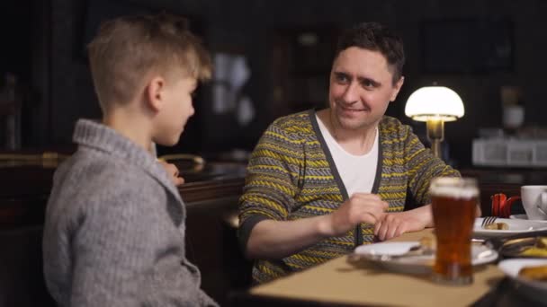 Père souriant serrant la main d'un fils adolescent assis dans un restaurant à l'intérieur. poignée de main au ralenti de l'homme caucasien heureux positif et garçon à l'intérieur. Unité familiale et concept de confiance. — Video