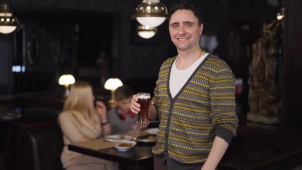 Portrait d'homme heureux avec une pinte de bière geste pouce levé en regardant la caméra sourire. Positif confiant père caucasien mari dîner avec la famille dans le restaurant publicité alcool. Mouvement lent. — Video