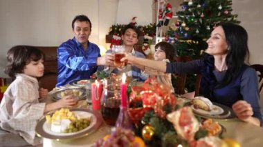 Neşeli mutlu aile meyve suyu bardaklarını tokuşturarak Noel 'de oturma odasında yemek yerken. Olumlu Orta Doğulu erkek ve beyaz kadın evde yeni yılı kutluyorlar..