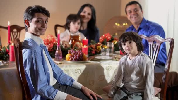 Adolescentes sonrientes positivos y pequeños hermanos de Oriente Medio mirando a la cámara sonriendo con un hermano gemelo borroso y un par de padres de fondo. Familia feliz celebrando la Navidad juntos. — Vídeo de stock