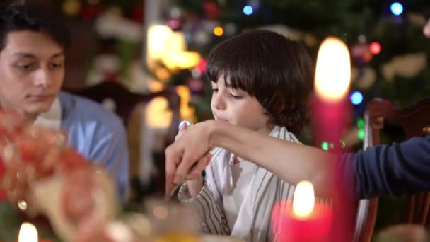 Közel-keleti fiú íze édes karácsonyi kenyeret ül a családdal vacsoraasztalnál nyaralás. Portré bájos aranyos gyerek élvezi Újévi ünneplés tizenéves testvér és anya beltéri. — Stock videók