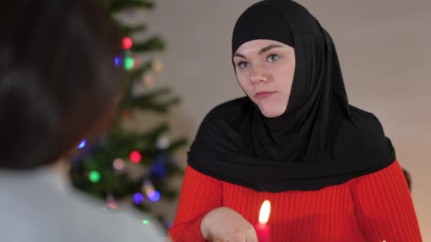 Porträtt av charmig ung kvinna i hijab prata med vän äta druva på julafton hemma inomhus. Vacker säker vit dam firar nyår dela skvaller med vän. — Stockvideo