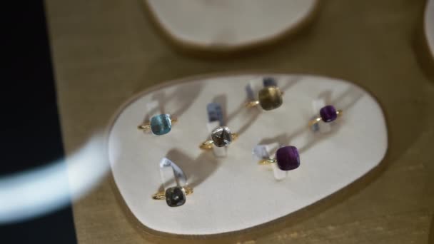 Gouden ringen met edelstenen binnenshuis in juwelierszaak close-up. Assortiment dure luxe sieraden op vitrine achter glas. Langzame beweging. — Stockvideo