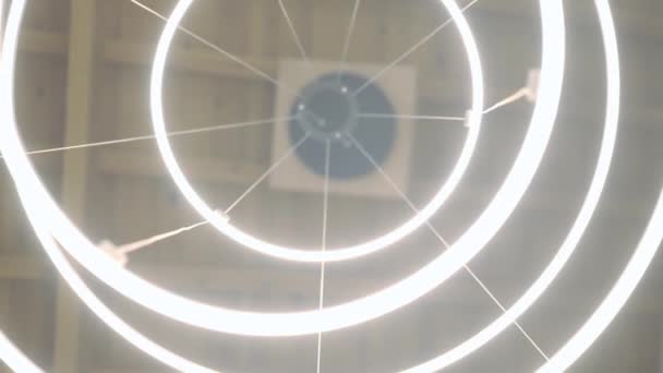 Onderaanzicht elegante verlichte kroonluchter hangend aan plafond binnen. Close-up ronde cirkels schitteren met koud licht in huis of winkel. Live camera draait in slow motion. — Stockvideo