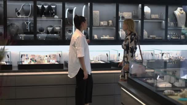 Wide shot slim elegant buyer and confident seller walking in jewellery store talking in slow motion. Side view portrait beautiful Caucasian women choosing luxurious accessories indoors in shop. — Stock Video