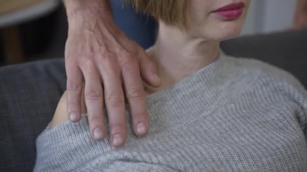 Unrecognizable slim young woman touching male hand on shoulder close-up. Sad upset Caucasian lady sitting on couch at home indoors supported by husband boyfriend. Unity and endorsement. — Stock Video