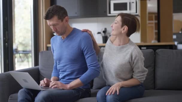 Busy concentrated man messaging online ignoring woman sitting down on couch in living room. Portrait of displeased Caucasian husband annoyed with spouse distracting from remote working. — Stock Video