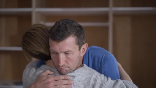 Zbliżenie mężczyzna przytula kobietę z niemiłosnym wyrazem twarzy myśląc. Portret zdezorientowanego chłopaka białego męża z żoną w domu. Koncepcja wątpliwości i uczuć. — Wideo stockowe