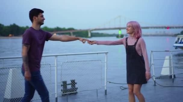 Junge fröhliche Millennial-Paare tanzen abends auf einem städtischen Damm und treffen sich im Freien. Glücklich lächelnde kaukasische Freund und Freundin genießen Freizeit in der Stadt. Konzept Liebe und Individualität. — Stockvideo