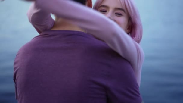 O tânără frumoasă și fericită, cu păr roz, îmbrățișând un bărbat cu valuri albastre de apă pe fundal. Loving subțire fermecător Caucazian prietena care se bucură de întâlnire cu prietenul în aer liber pozând. — Videoclip de stoc