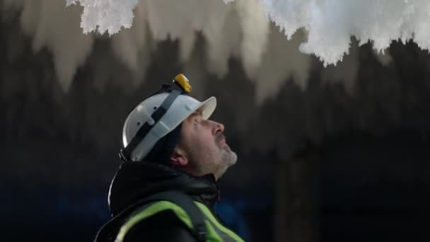 Eccitato uomo barbuto guardando intorno a gelo neve in grotta di ghiaccio all'aperto. Fiducioso viaggiatore adulto caucasico in casco con torcia ammirando la bellezza della natura. — Video Stock