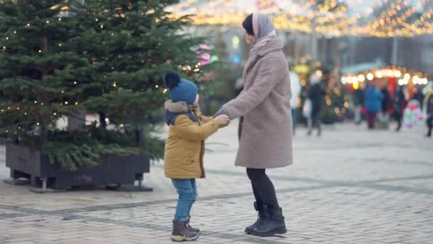 Široký záběr radostné blízkovýchodní matka a syn tančí ve zpomaleném filmu venku na Silvestra. Šťastná mladá žena se baví s chlapcem na Vánoce ve městě. Životní styl a rodinný koncept. — Stock video