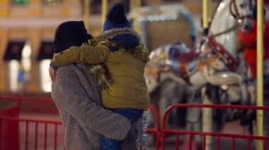 Ortadoğulu genç bir kadının ellerinde akşam vakti dışarıda Noel atlıkarıncasını hayranlıkla seyreden küçük bir çocuk. Neşeli hiperaktif evlat, yeni yılın tadını çıkartıyor. Annesiyle birlikte. Aile eğlencesi..