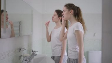 Yan görünüşlü ikiz kardeşler sabahları evdeki banyoda dişlerini fırçalıyorlar. Güzel, ince, beyaz kadınlar içeride güzellik ve sağlıkla ilgileniyorlar. Hijyen ve rutin konsept.