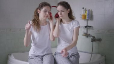 Banyo küvetinde oturmuş kulaklıkla müzik dinleyen tek yumurta ikizi kardeşler. İnce, çekici beyaz kadın portresi sabah evde hobi ediniyor..
