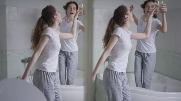 Radosny taniec dwóch zrelaksowanych bliźniaczek w łazience w domu. Wesoła piękna szczupła biała kobieta w piżamie tańcząca w weekend w domu. Koncepcja siostrzana. — Wideo stockowe