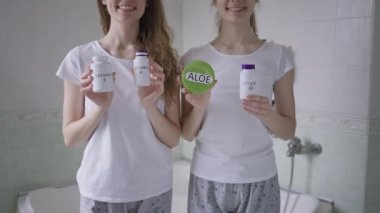 Banyoda pijama giymiş, elinde vitaminlerle gülümseyen tanınmamış genç kadınlar. Kafkasyalı olumlu ikiz kardeşler sabahları evde organik haplar satıyorlar..