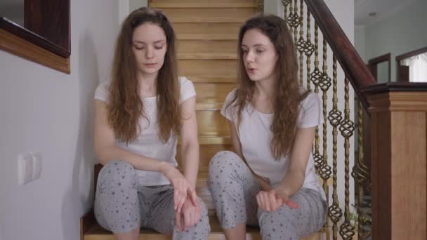 Hermanas gemelas enojadas hablando gritando discutiendo sentadas en las escaleras como una mujer dejando a otra suspirando. Concepto de diferencia de individualidad y conflictos familiares. — Vídeo de stock