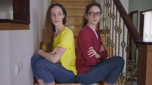 Argumenterad smal vacker identiska kvinnor sitter tillbaka till tillbaka på trappor tänkande suckande. Charmigt självsäkert elegant dam och nörd syskon inomhus. Begreppet individualitet. — Stockvideo