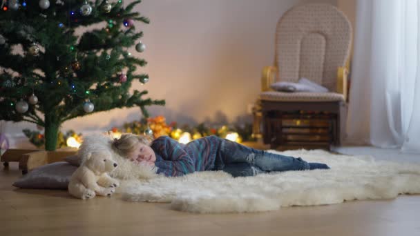 Ampla tiro descontraído despreocupado menino caucasiano bonito deitado na árvore de Natal na sala de estar fechando os olhos adormecendo. Criança encantadora esperando milagre na véspera de Ano Novo em casa. Conceito de feriados. — Vídeo de Stock