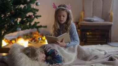 Sevgili küçük kız kardeşim yeni yıl arifesinde evde erkek kardeşime kitap okuyor. Oturma odasındaki Noel ağacında kapalı bir salonda güzel beyaz bir kız ve erkek çocuğunun portresi. Mutluluk ve rahatlık.