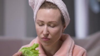 Saç havlusuyla yeşil salata yaprağı içen tatminsiz genç bir kadın. Evinde sabahları diyet yapan mutsuz beyaz kadın portresi. Kadınlık ve öz disiplin kavramı.