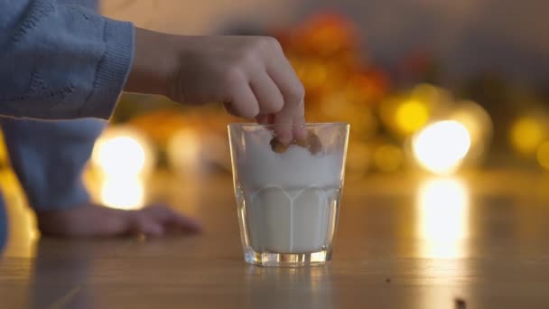 白い牛乳と女の子とのクローズアップガラスは、飲み物でクリスマスクッキーを浸漬手。認識できない白人の子供は、大晦日に自宅で甘いデザートの味を楽しむ. — ストック動画