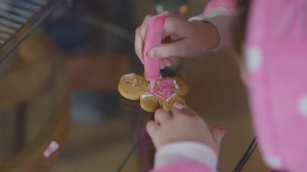 Közelkép mézeskalács süti kis női kezekkel, desszert rózsaszín királyi cukormázzal. Felismerhetetlen kaukázusi kislány készül édes ízletes hagyományos karácsonyi ételek beltéri. — Stock videók