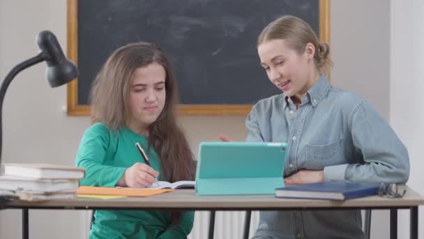 Alegre mujer caucásica y pequeña persona haciendo gestos de alta cinco sentado en el escritorio hablando en el aula. Estudiante inteligente feliz positivo y tutor regocijándose en interiores estudiando. Educación y alegría. — Vídeos de Stock