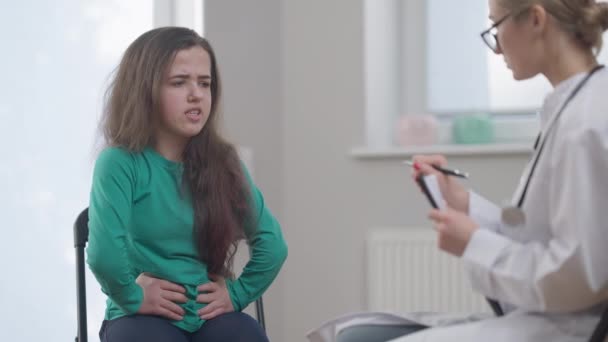 Paciente femenina que habla quejándose de dolor abdominal síntomas de indigestión. Pequeña persona caucásica consultando médico profesional en gafas en el hospital. Concepto de enfermedad y medicina. — Vídeo de stock