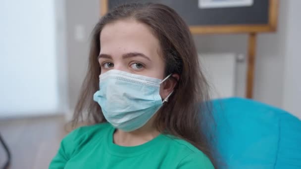 Маленька людина в коронавірусі дивиться на камеру з серйозним виразом обличчя. Портрет молодої кавказької жінки у приміщенні на ізоляції від пандемії Ковід-19.. — стокове відео