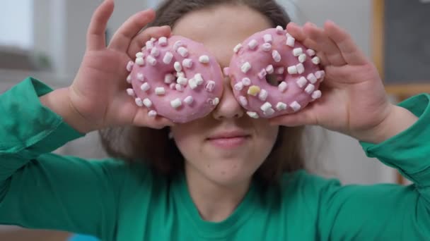 Close-up alegre pequena pessoa brincando com doces deliciosos donuts mostrando vista frontal língua. Retrato de mulher caucasiana alegre se divertindo dentro de casa colocando sobremesa saborosa nos olhos sorrindo. — Vídeo de Stock