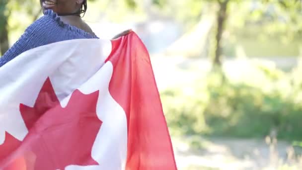Onherkenbare Afro-Amerikaanse lachende vrouw draaiend met Canadese vlag in het zonlicht in het zomerpark. Happy zelfverzekerde ontspannen dame poseren met nationaal symbool buiten in de zon. — Stockvideo
