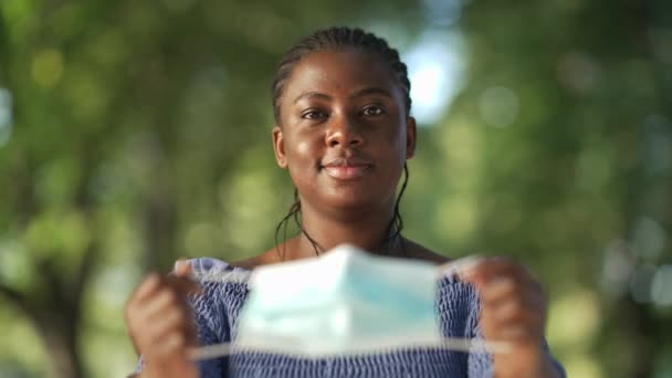 Vooraanzicht portret serieuze Afro-Amerikaanse vrouw zet coronavirus gezichtsmasker op kijkend naar camera. Zelfverzekerde dame die poseert in het zomerpark bij de Covid-19 pandemie. Nieuw normaal. — Stockvideo