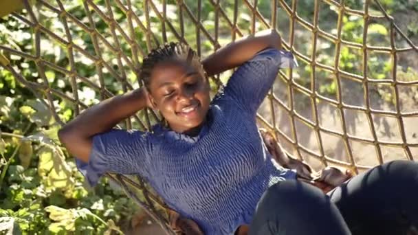 Visão superior feliz sorrindo mulher afro-americana com os olhos fechados deitado na rede desfrutando de lazer. Retrato de senhora millennial plus-size confiante descansando ao sol no dia de verão ao ar livre. Devagar. — Vídeo de Stock