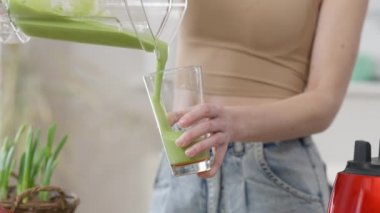 Tanınmayacak kadar zayıf, beyaz bir kadın blender bardağından yeşil sağlıklı vejetaryen içeceği dolduruyor. Evde sabahları sağlıklı bir detoks kokteyli içen kendine güvenen bin yıllık bir bayan..