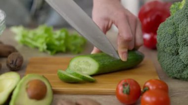 Mutfakta salatalığı bıçakla doğrayan yakın plan kadın. Evde sağlıklı vejetaryen salatası pişiren tanımlanamayan ince, beyaz bir bayanın elleri..