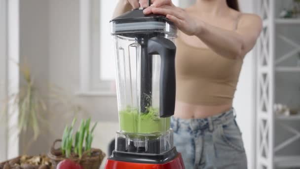 Ung oigenkännlig kvinna blandar grön hälsosam detox vegan cocktail i mixer hemma. Smal kaukasisk tusenårig dam förbereder hälsosam vegetarisk dryck i köket inomhus. — Stockvideo
