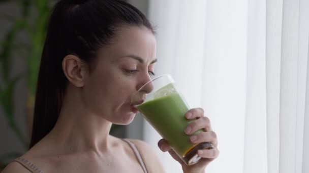 Close-up retrato jovem satisfeito bela mulher bebendo saboroso smoothie desintoxicação dentro de casa olhando pela janela. Feliz caucasiano milenar vegetariano senhora desfrutando saudável bebida verde em casa. — Vídeo de Stock