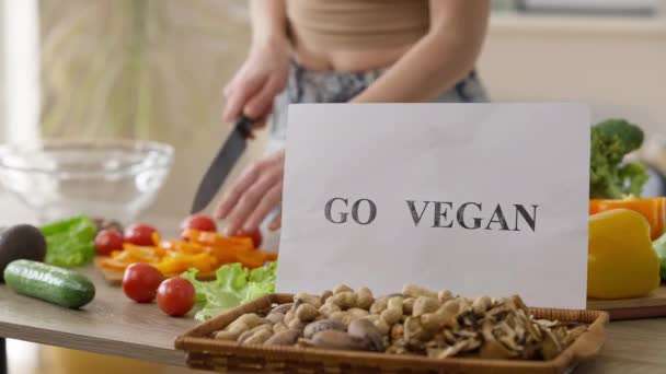 Close-up Vá vegan em nozes de amêndoa com mulher irreconhecível picando pimentão para salada no fundo. Jovem magro caucasiano senhora cozinhar comida saudável em casa dentro de casa. — Vídeo de Stock