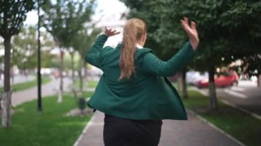 Arka plan portresi mutlu, mutlu, obez bir kadın dans ediyor, kaldırımda keyifle yürüyor. Neşeli beyaz kadın şehir sokaklarında ağır çekimde eğleniyor..