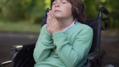 Canlı kamera, gözleri kapalı sakat bir çocuğun yüzünü tekerlekli sandalyedeki legrest 'e çeviriyor. Yaz parkında beyaz bir çocuğun güzel görünmesini umarak poz verdim. Din ve sakatlık.