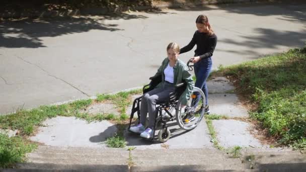Szeroki strzał zdenerwowany nastolatek kaukaski i niepełnosprawny przyjaciel na wózku inwalidzkim stojący na schodach bez rampy na zewnątrz odchodząc. Piękna empatyczna dziewczyna dbająca o sparaliżowanego przyjaciela pchającego urządzenie. — Wideo stockowe