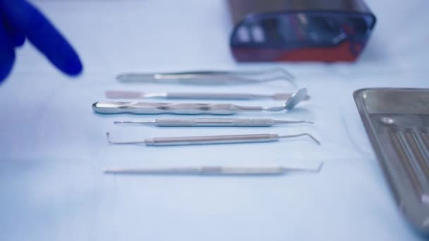 男性の手で病院のテーブルの上に歯科用ツールは、ゆっくりと動きに残して口ミラーを取る機器を選択手袋で。屋内オフィスでの認識できないプロの歯科医MD. — ストック動画