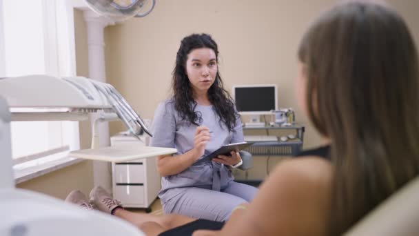 若い美しい女性歯科医の肖像室内で椅子に座って10代の患者とスローモーションで話しています。正の白人女性は病院でティーンエイジャーをコンサルティング.医学と健康の概念. — ストック動画