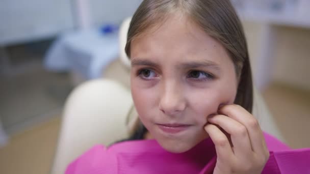 Zbliżenie nastolatka narzeka ból zęba pochylając się jako kobieta ręka za pomocą lustra usta badania jamy ustnej w zwolnionym tempie. Portret smutnego pacjenta rasy kaukaskiej na krześle dentystycznym w klinice w pomieszczeniach. — Wideo stockowe