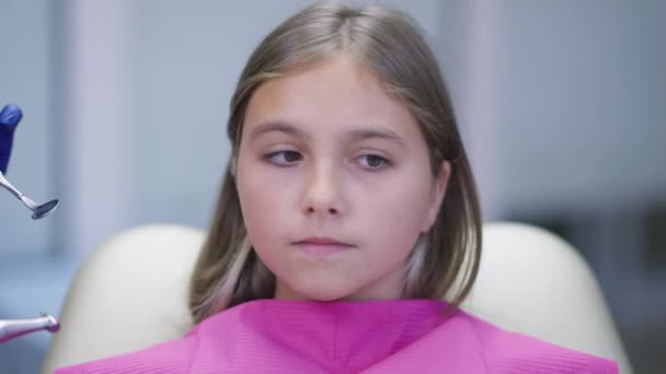 Huvudskott porträtt rädd kaukasiska flicka täcker ansiktet med händerna som dentala verktyg närmar sig i slow motion runt. Närbild porträtt skrämd patient i tandläkare stol på sjukhus. — Stockvideo