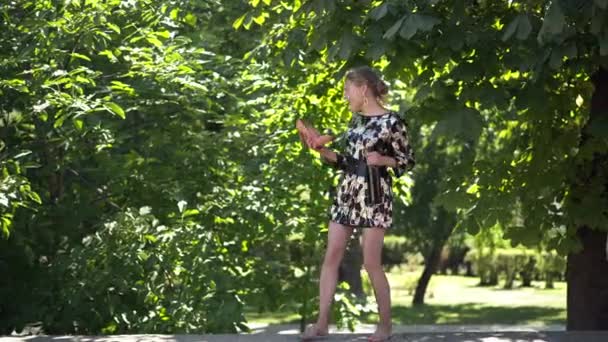 Onvoorzichtige blanke boze dronken vrouw die danst met een wijnfles die een telefoongesprek imiteert in schoen. Breed shot portret van gebroken hart jonge mooie feestganger buiten in zonnig park. — Stockvideo